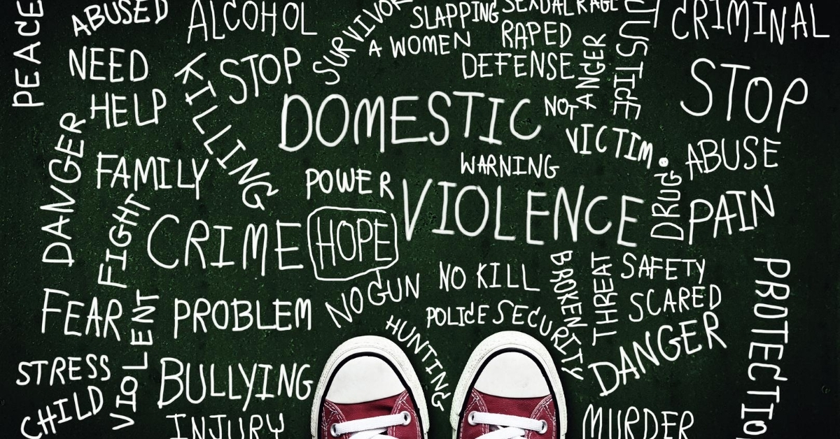 Person wearing shoes looking down at a chalkboard with words related to violence